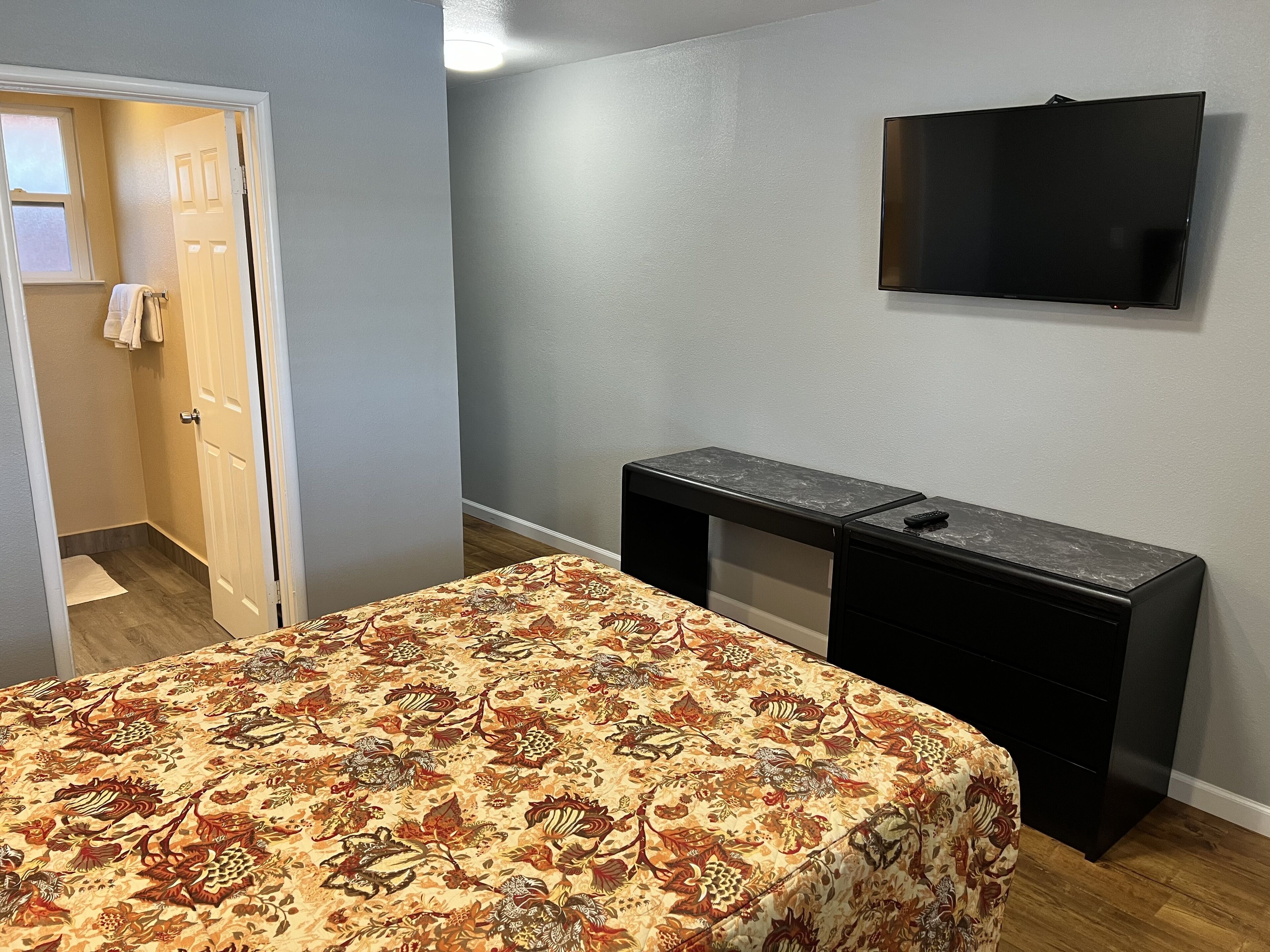 Quarto com uma cama, escrivaninha e televisão na parede.