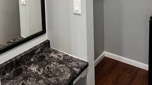 Ein Badezimmer mit Marmorplatte, einer weißen Wand mit strukturierter Oberfläche, einem Handtuchhalter und einem Wandheizkörper.