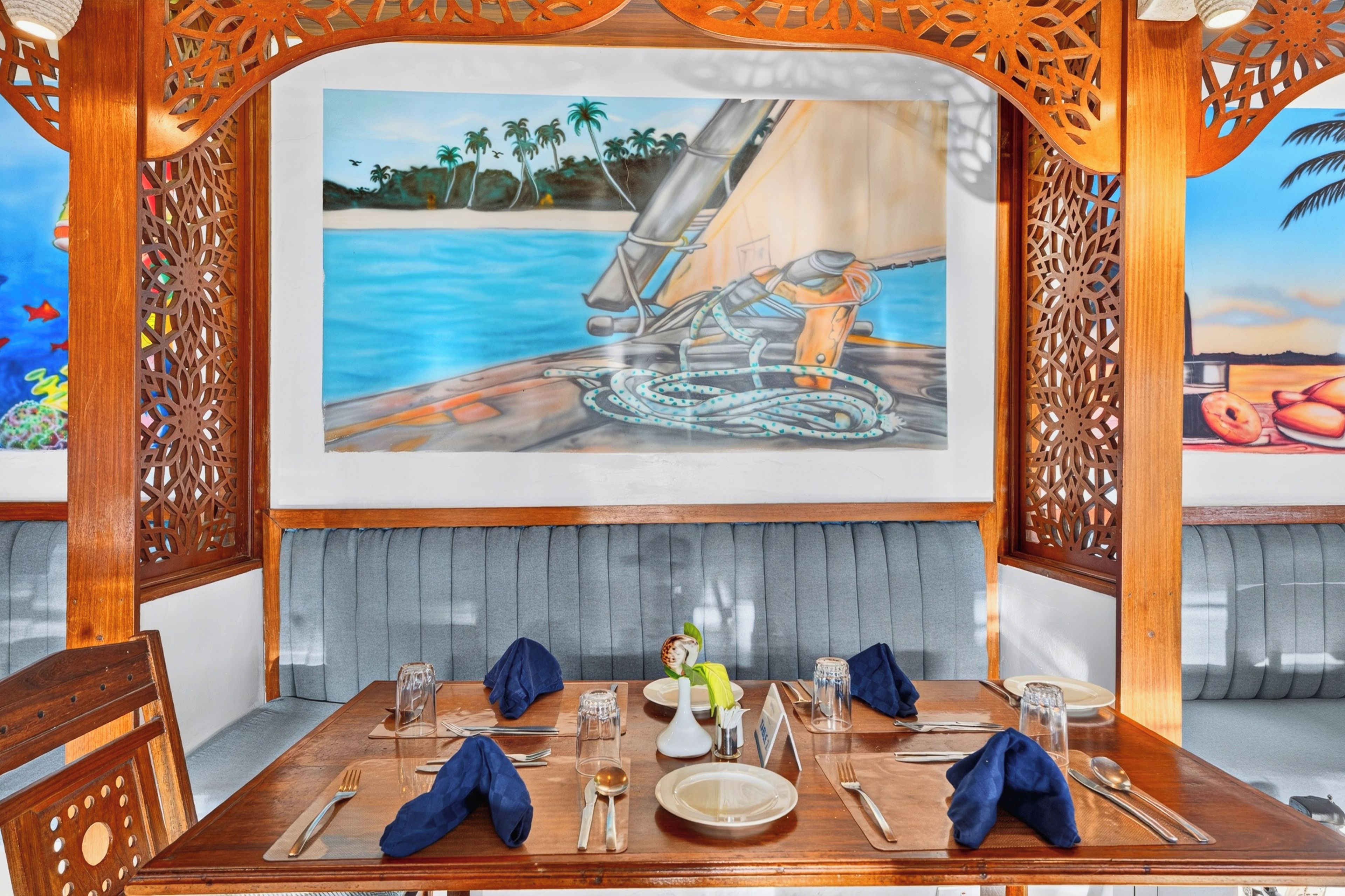 A dining area with a table set for two, a painting of a sailboat on the wall, and a view of the ocean.