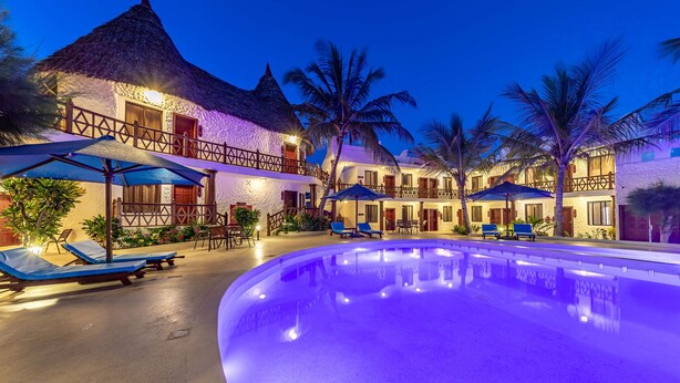 Resort com piscina, espreguiçadeiras e edifícios com telhados de palha.