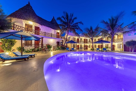 A resort with a swimming pool, lounge chairs, and thatched-roof buildings.