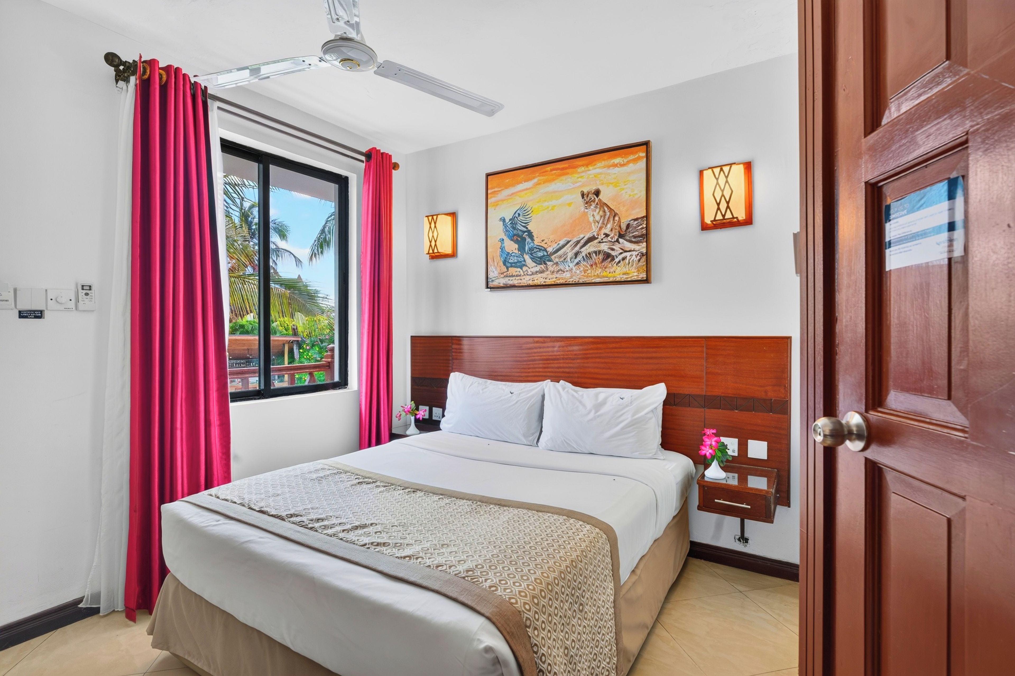 Une chambre d’hôtel avec un lit, une fenêtre avec des rideaux, un tableau au mur et une porte.