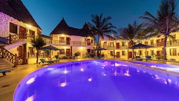 A resort with a swimming pool, thatched-roof buildings, and palm trees.