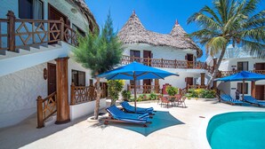 Um resort com piscina, espreguiçadeiras e edifícios com telhados de palha.