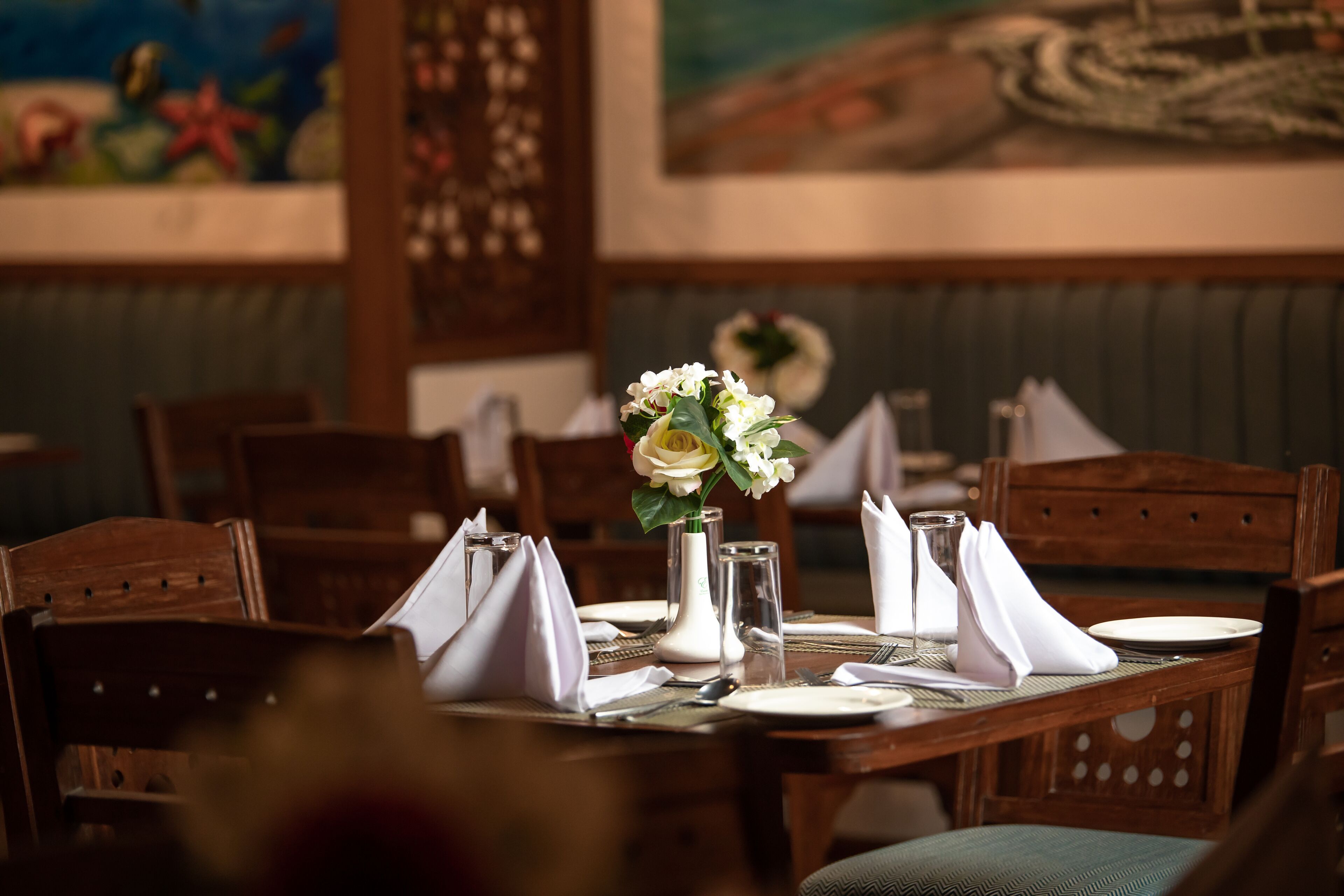 A dining table set with white napkins, a vase with flowers, and a glass.