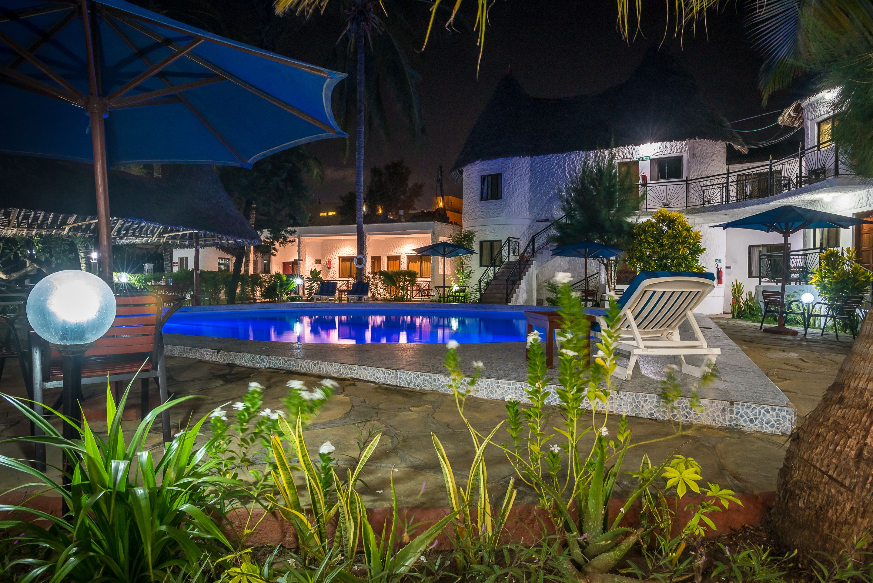 An outdoor pool area with lounge chairs and umbrellas, surrounded by plants and a stone pathway.
