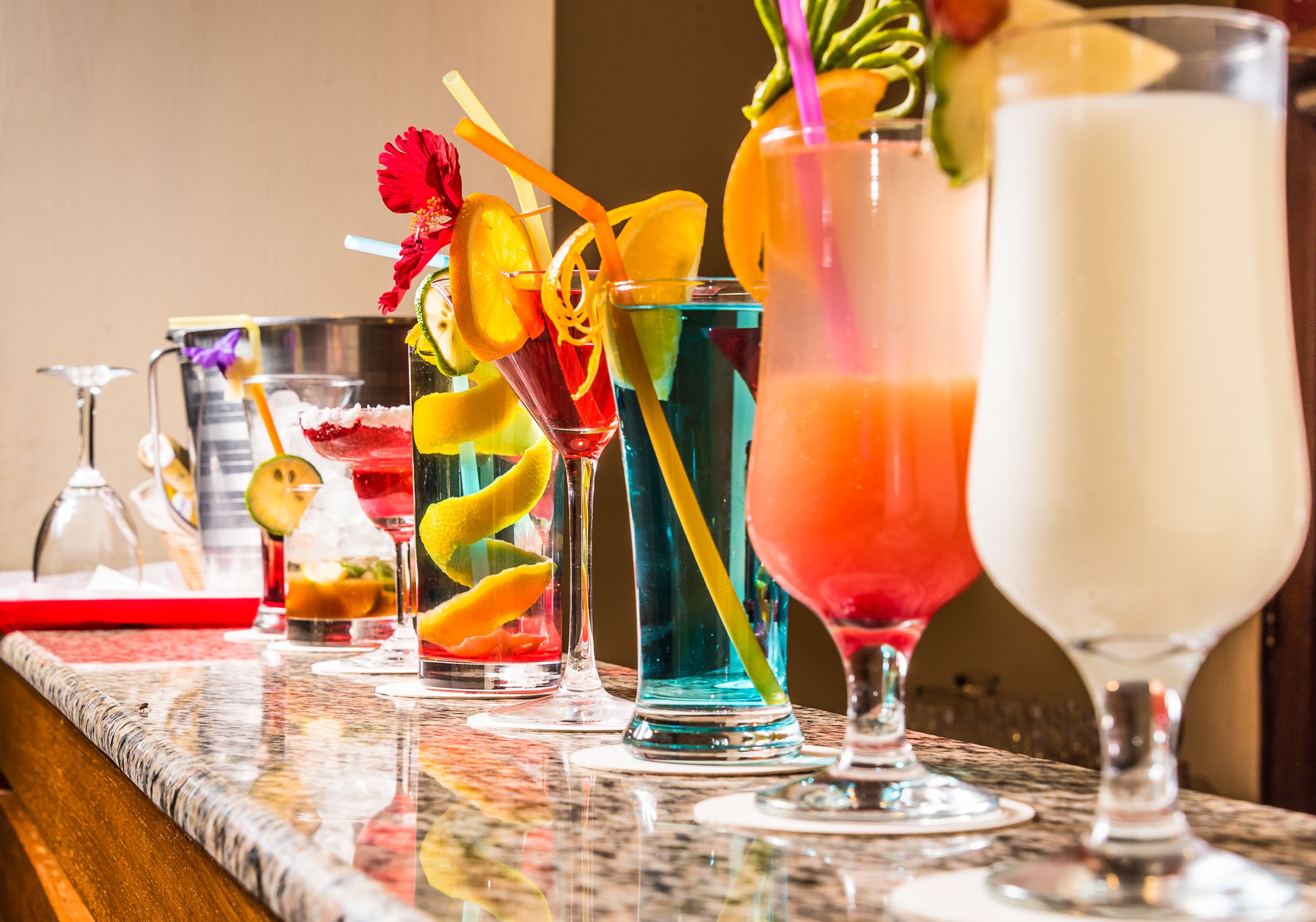 Zona de bar con varios cócteles, incluyendo una bebida roja con una rodaja de limón y una bebida azul con pajita.