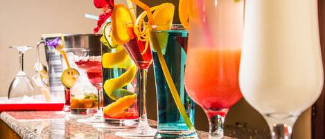 Zona de bar con varios cócteles, incluyendo una bebida roja con una rodaja de limón y una bebida azul con pajita.