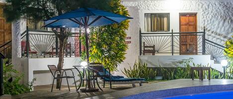 Zona junto a la piscina con un edificio blanco, mobiliario exterior y una escalera que lleva a un balcón.