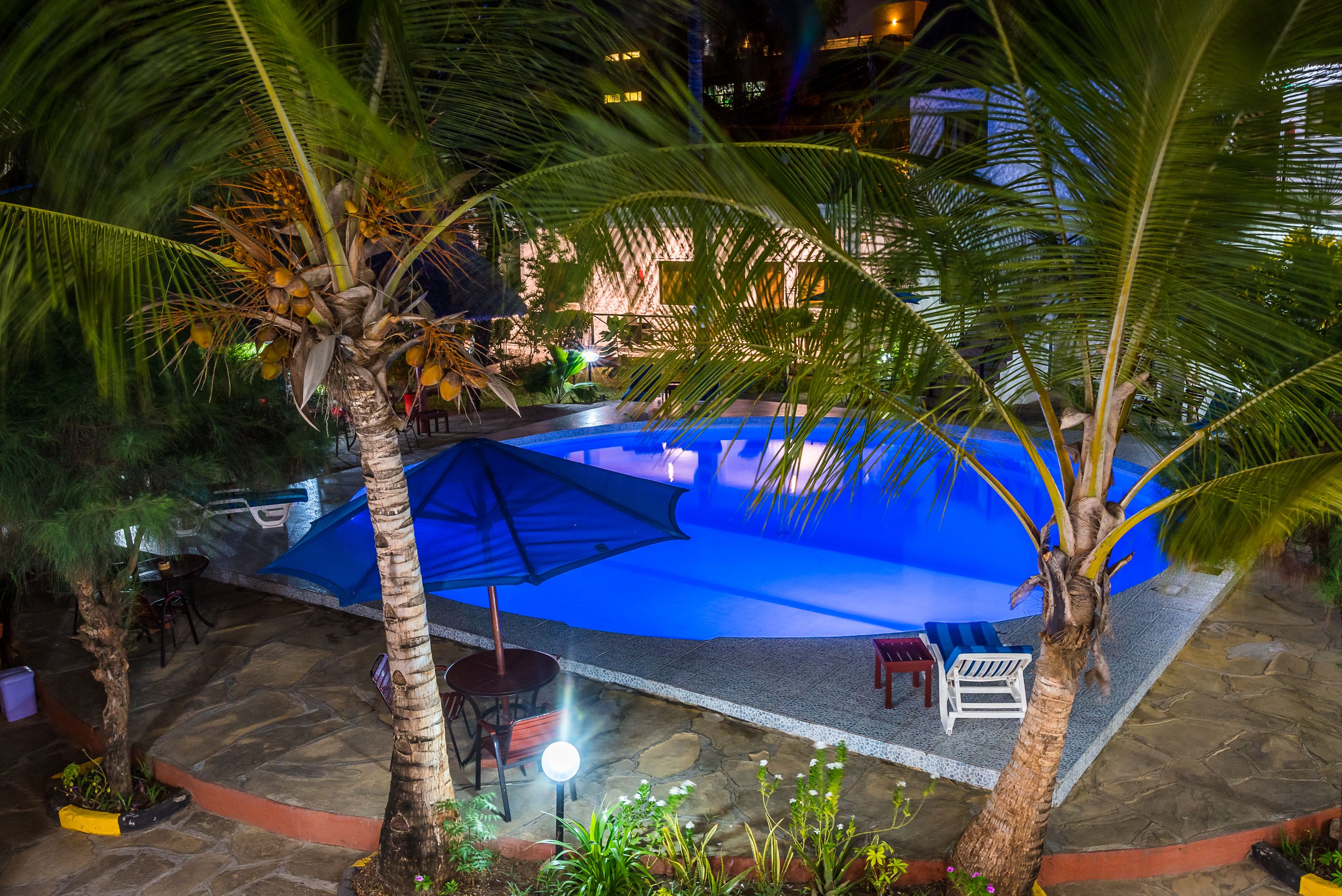 An outdoor pool area with a blue canopy, palm trees, and stone flooring.