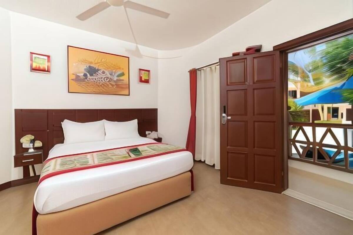 A hotel room with a bed, a nightstand, a ceiling fan, and a door leading to a balcony with a view.