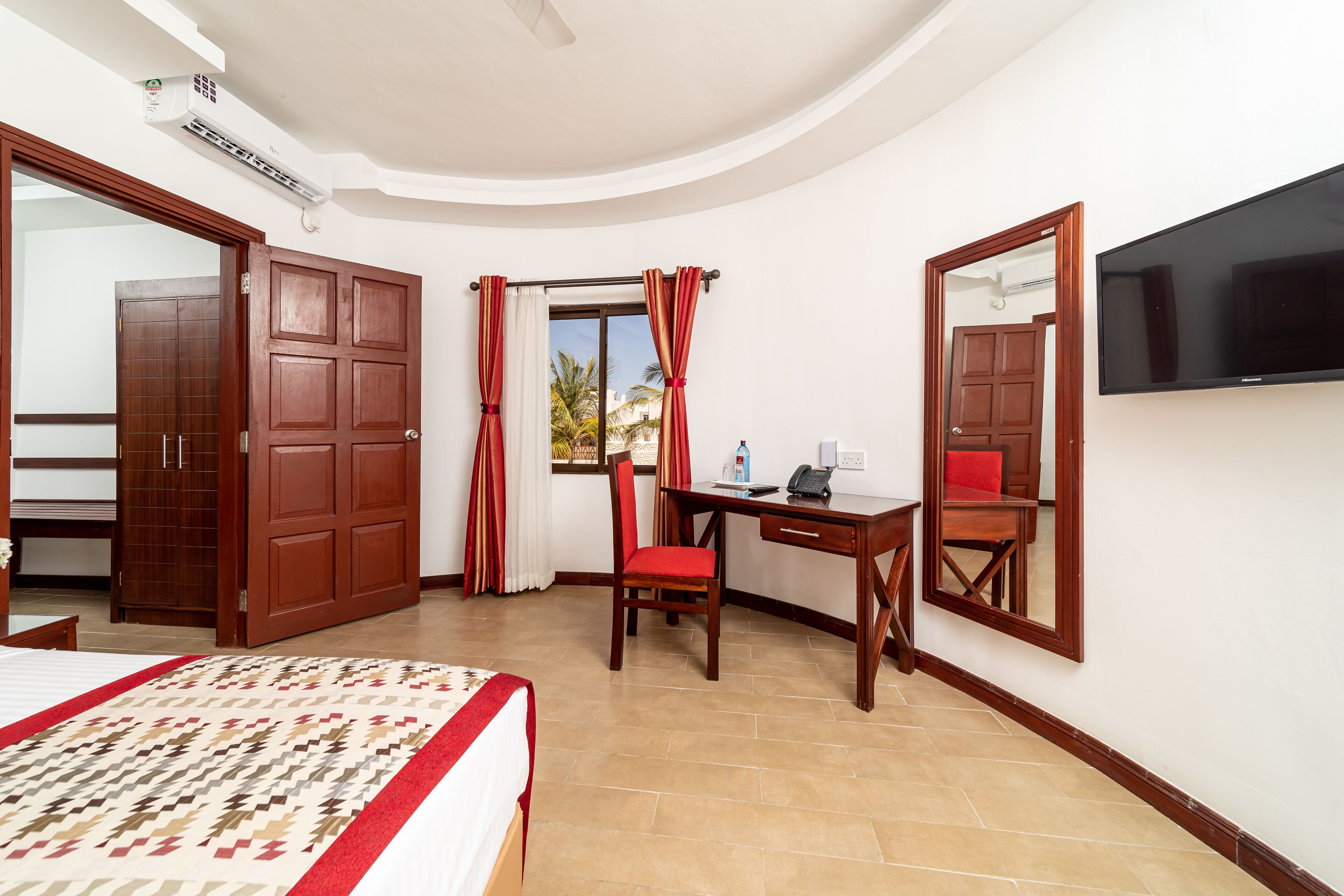 A hotel room with a bed, desk, chair, TV, and large mirror.