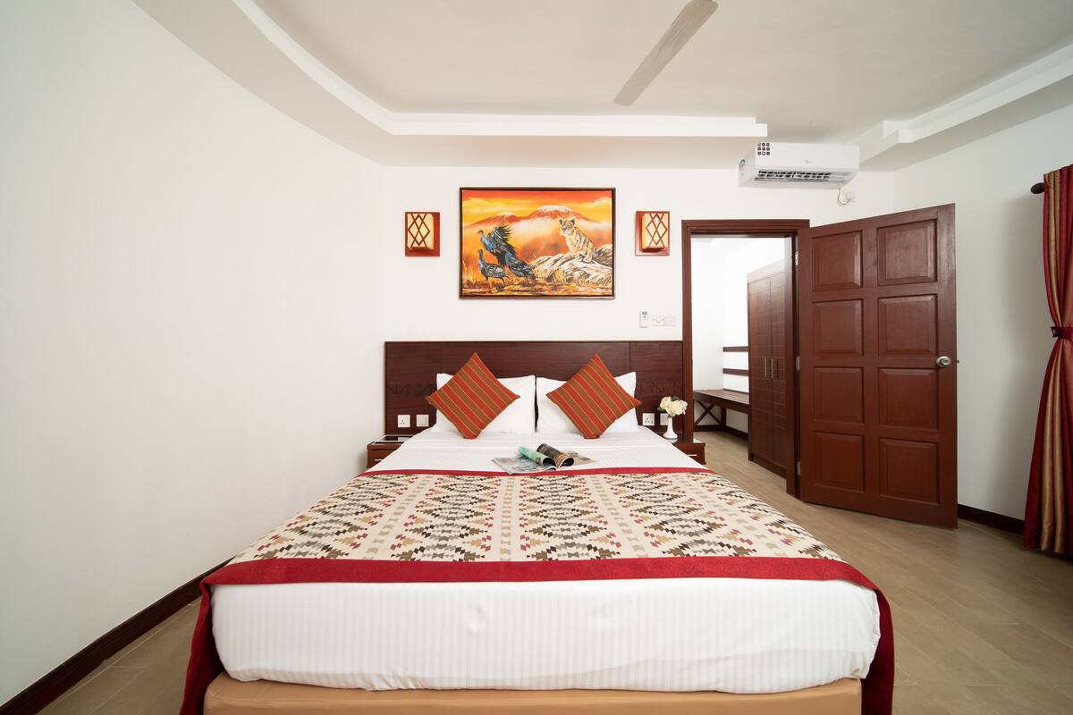 A hotel room with a large bed, a painting on the wall, and a wooden door.