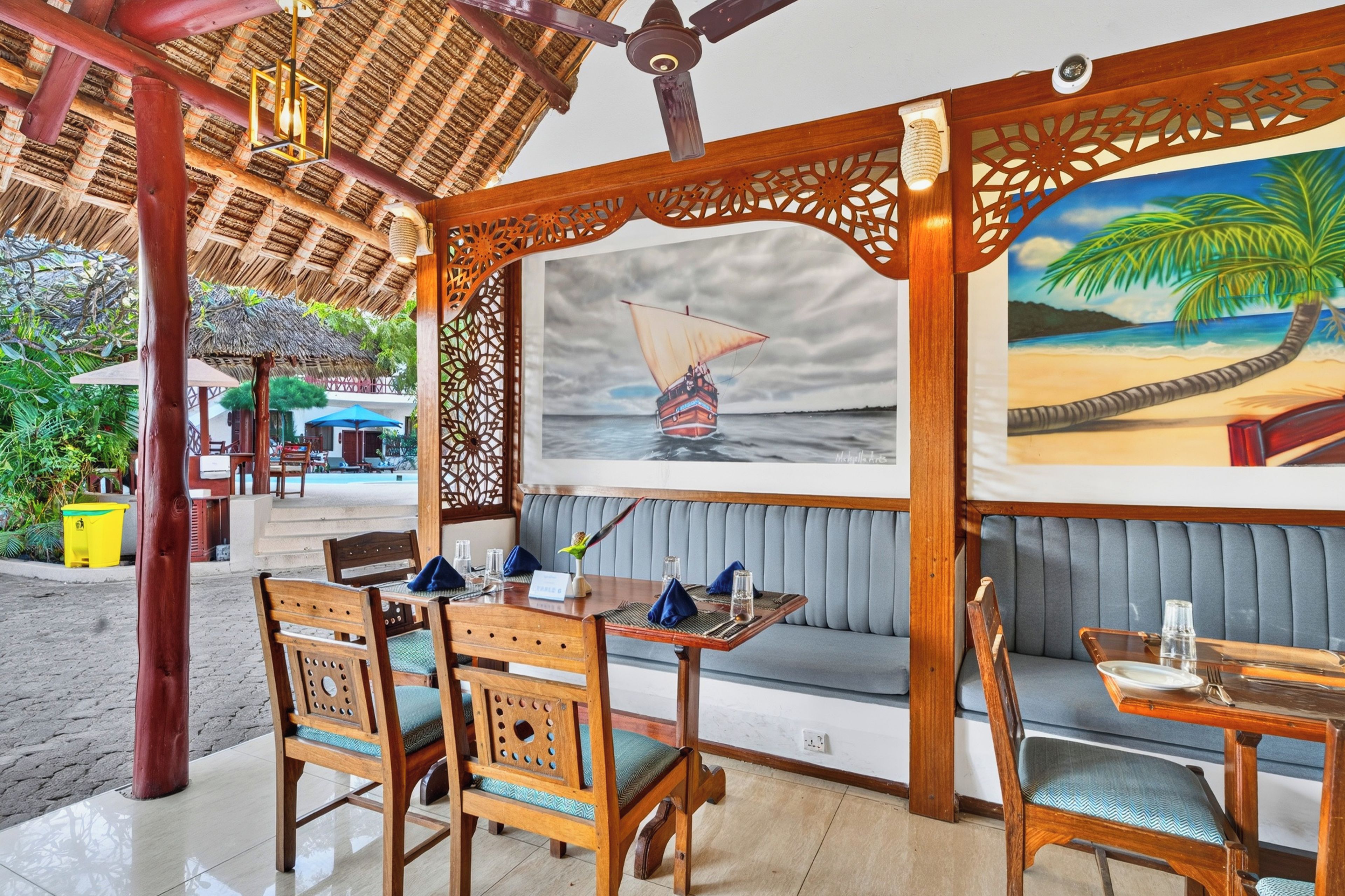 Un restaurante con muebles de madera, techo de paja y un cuadro de un velero.