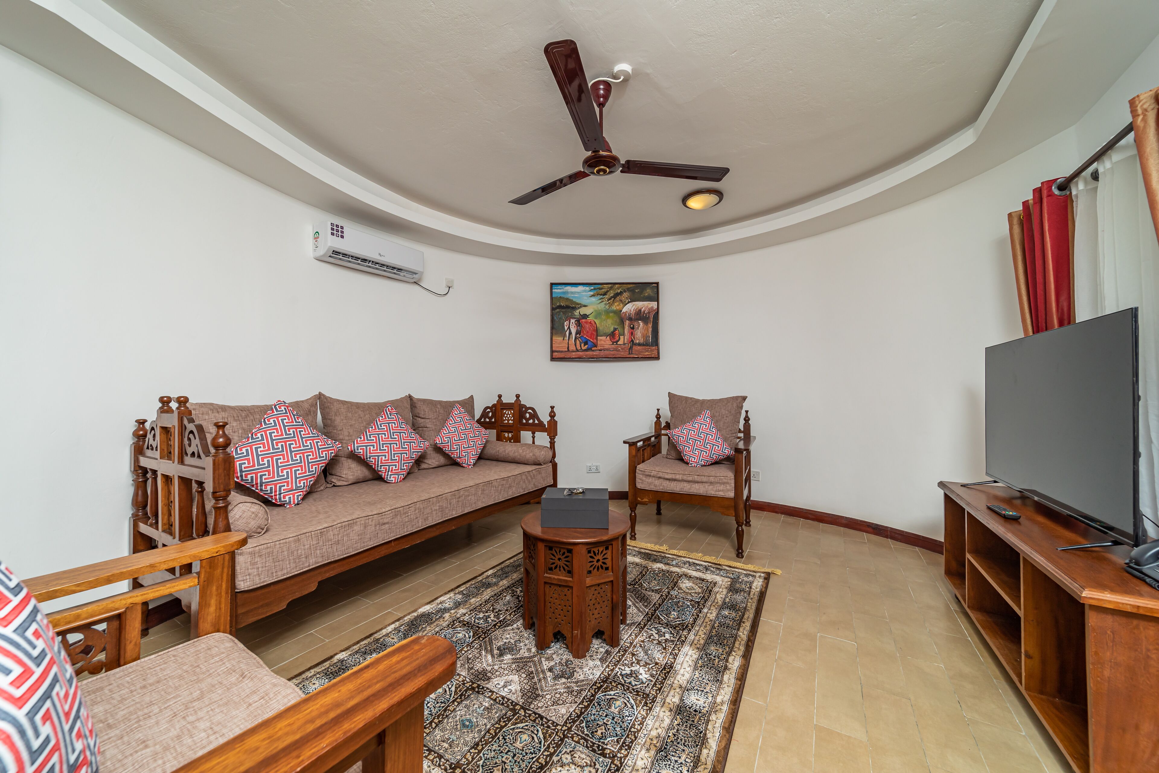 A living room with a sofa, chairs, a coffee table, a TV, and a ceiling fan.
