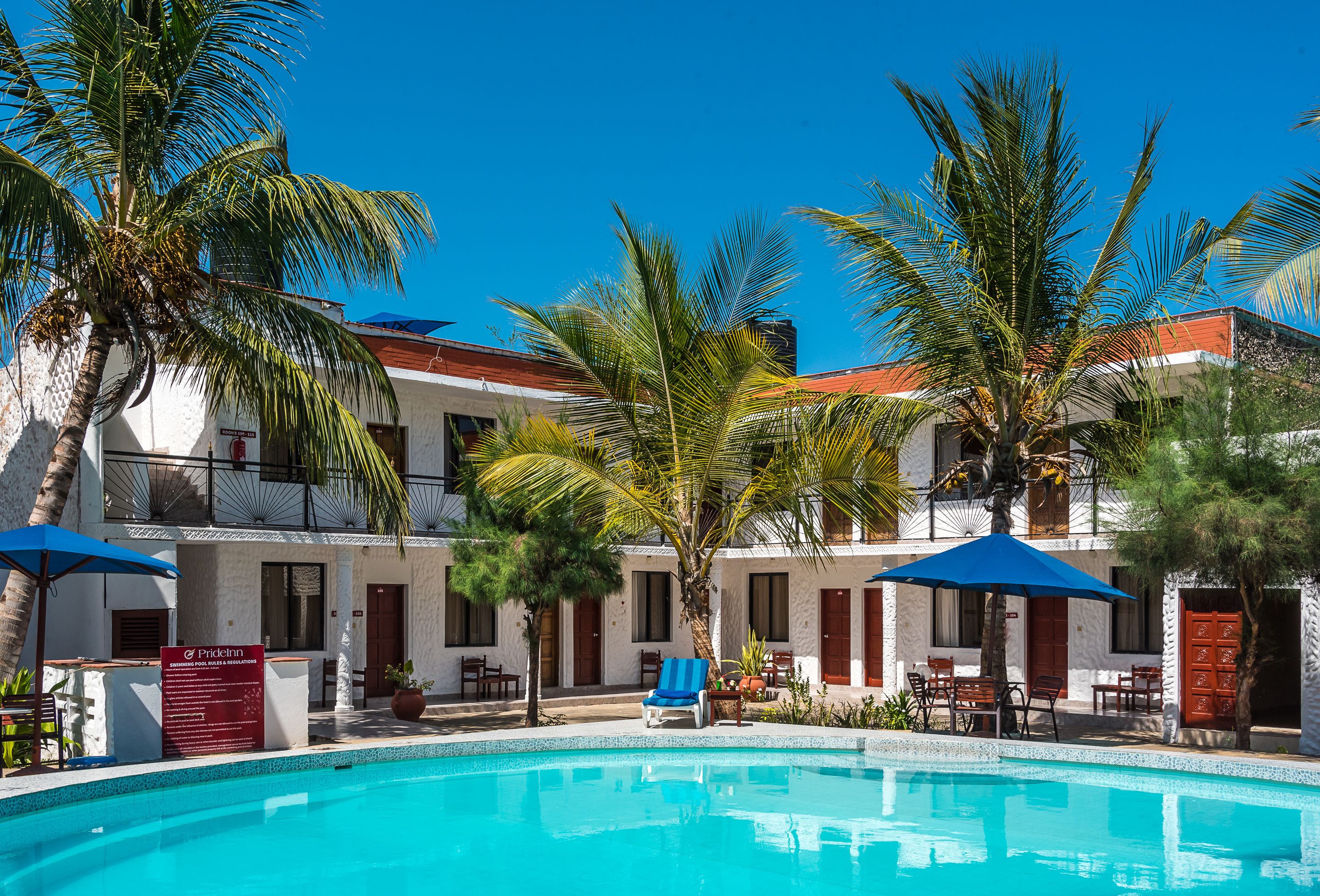A hotel with a swimming pool, palm trees, and outdoor seating areas.