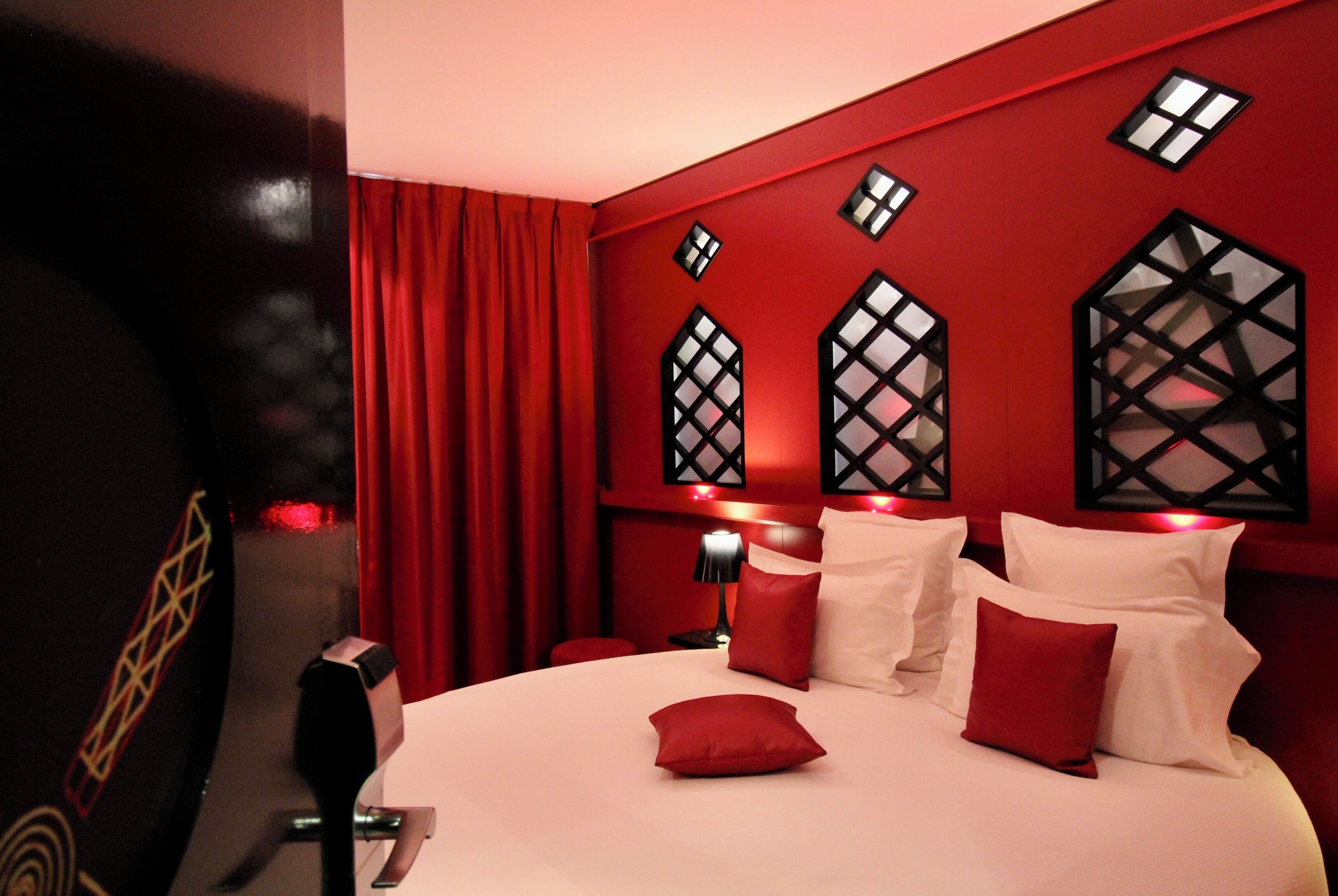 A hotel room with a large bed, red curtains, and decorative wall panels.