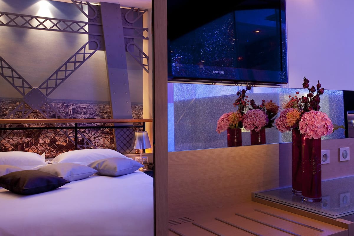 Una habitación de hotel con una cama, un televisor montado en la pared y un jarrón decorativo con flores.