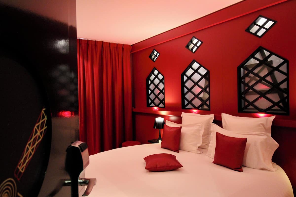 Habitación de hotel con una cama grande, cortinas rojas y paneles decorativos en la pared.