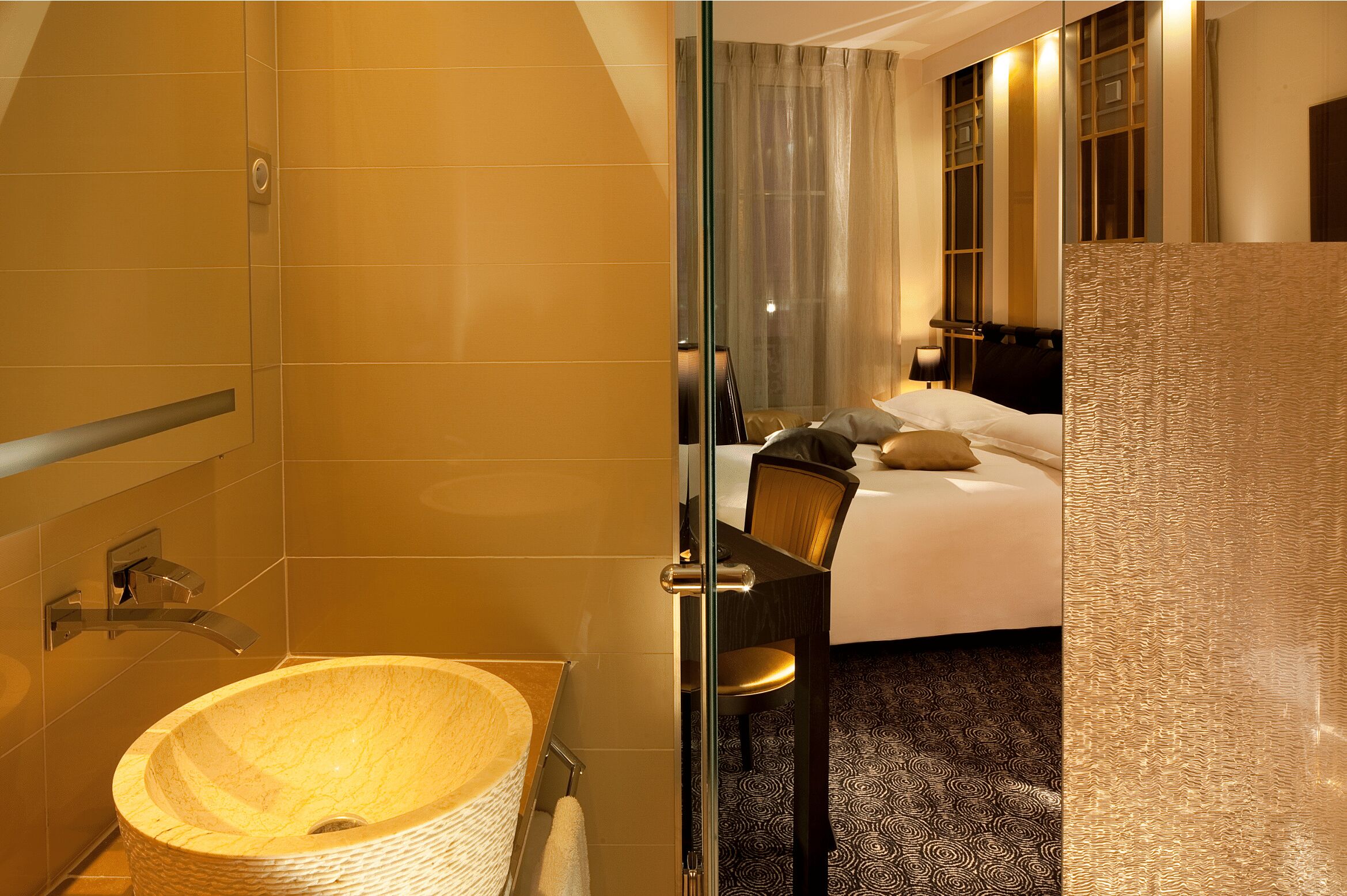 A hotel room with a large oval sink, a bed with a headboard, and a mirror reflecting the room.