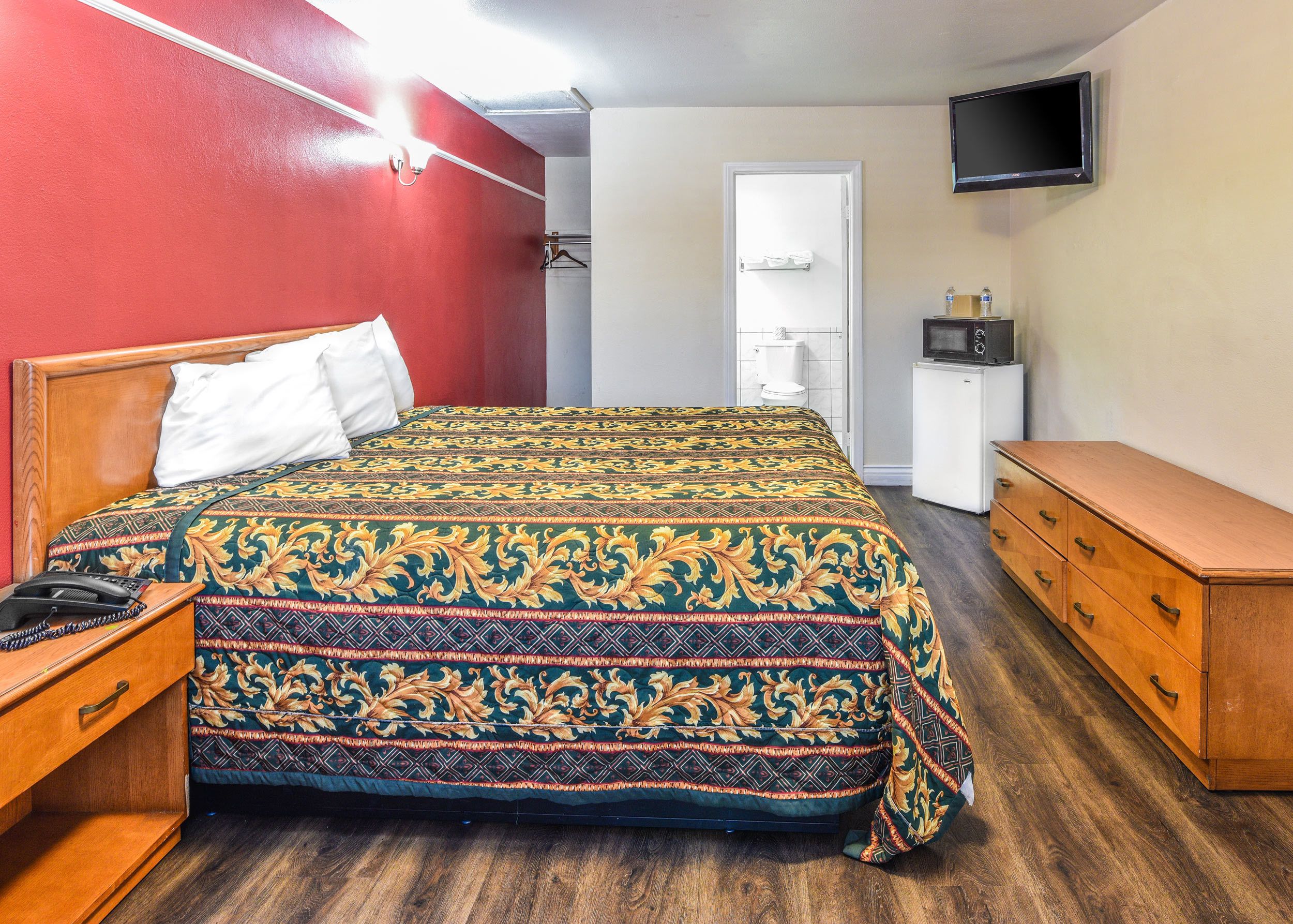 Una habitación de hotel con cama, cómoda de madera y televisor en la pared.