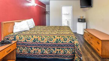 Una habitación de hotel con cama, cómoda de madera y televisor en la pared.