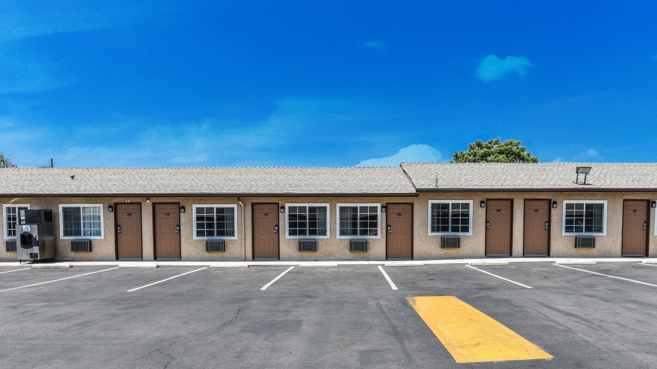 A motel with a row of rooms, each with a door and window, and a parking lot in front.