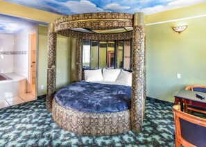Una cama redonda con dosel estampado en una habitación con alfombra estampada y vistas al baño.