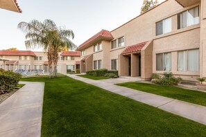 A row of beige buildings with red-tiled roofs, a well-maintained lawn, and a pathway leading to a pool area. - Indian Palms Vacation Club (Indio)