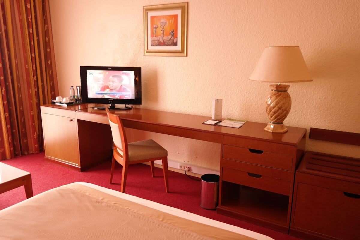 Ein Hotelzimmer mit einem Bett, einem Schreibtisch mit Computer, einem Stuhl, einer Lampe und einem Papierkorb.
