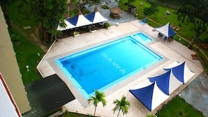 A swimming pool surrounded by palm trees and covered with blue and white canopies. - Hôtel SAWA (Douala)