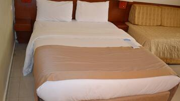Quarto de hotel com uma cama grande, uma cama menor e uma mesa de cabeceira com abajur.