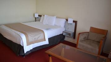 A hotel room with a bed, bedside tables, a chair, and a glass-top coffee table.