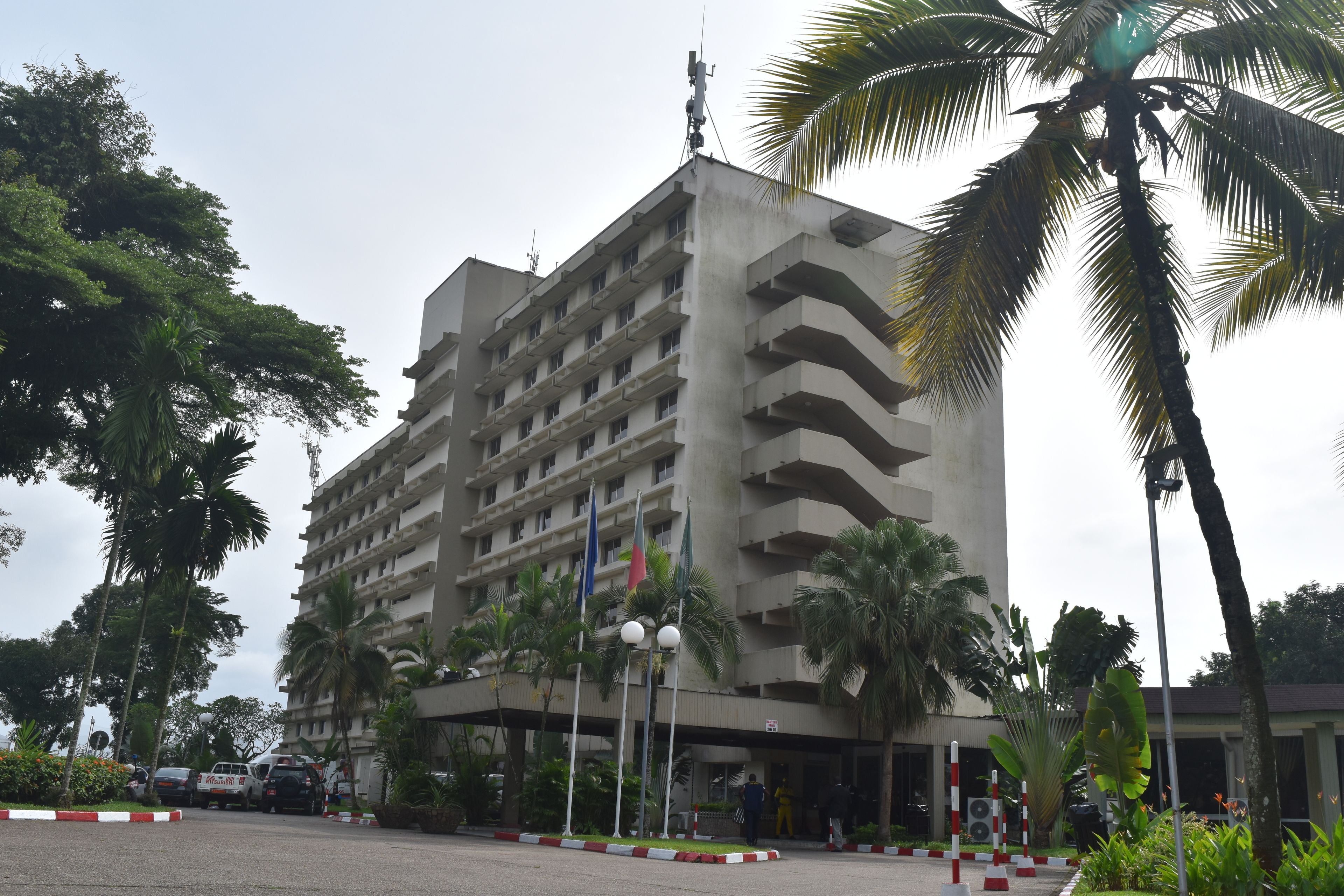 A multi-story hotel with a central courtyard, surrounded by palm trees and a parking area.