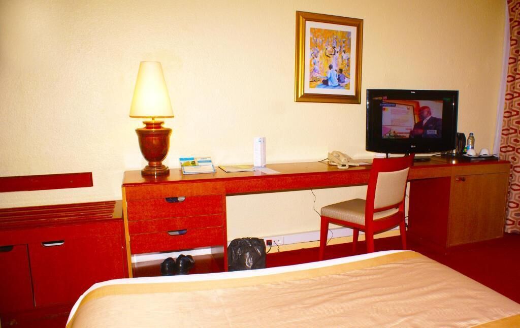 A hotel room with a bed, a desk with a lamp, a television, and a chair.