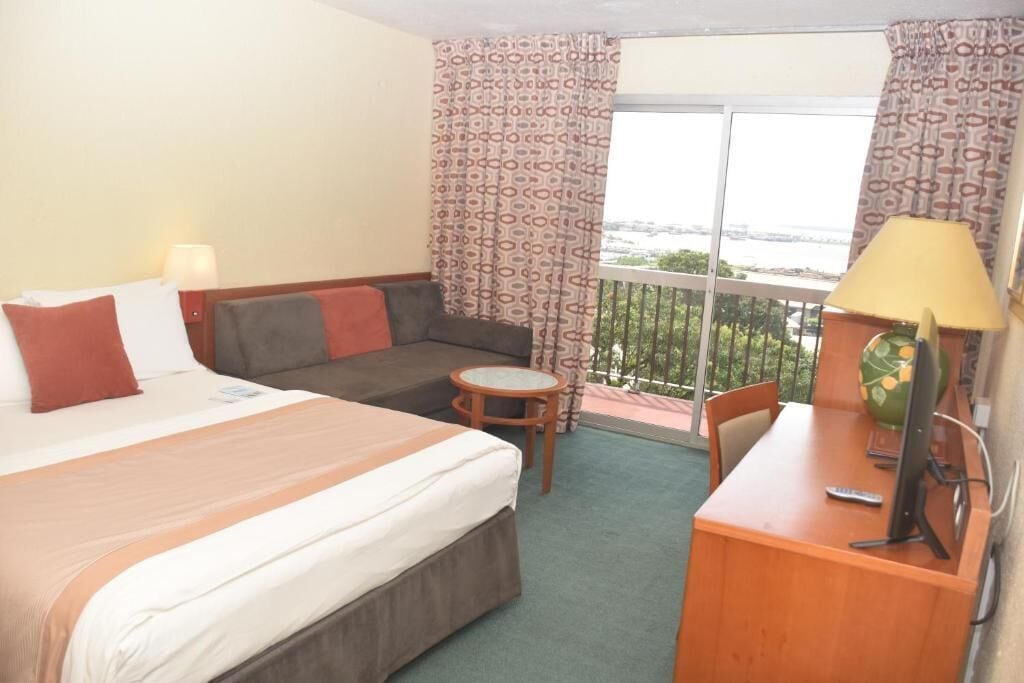 A hotel room with a bed, a sofa, a desk with a computer, and a small table.