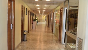A hallway with patterned floor tiles, wooden doors, and glass-fronted shops. - Hôtel SAWA (Douala)