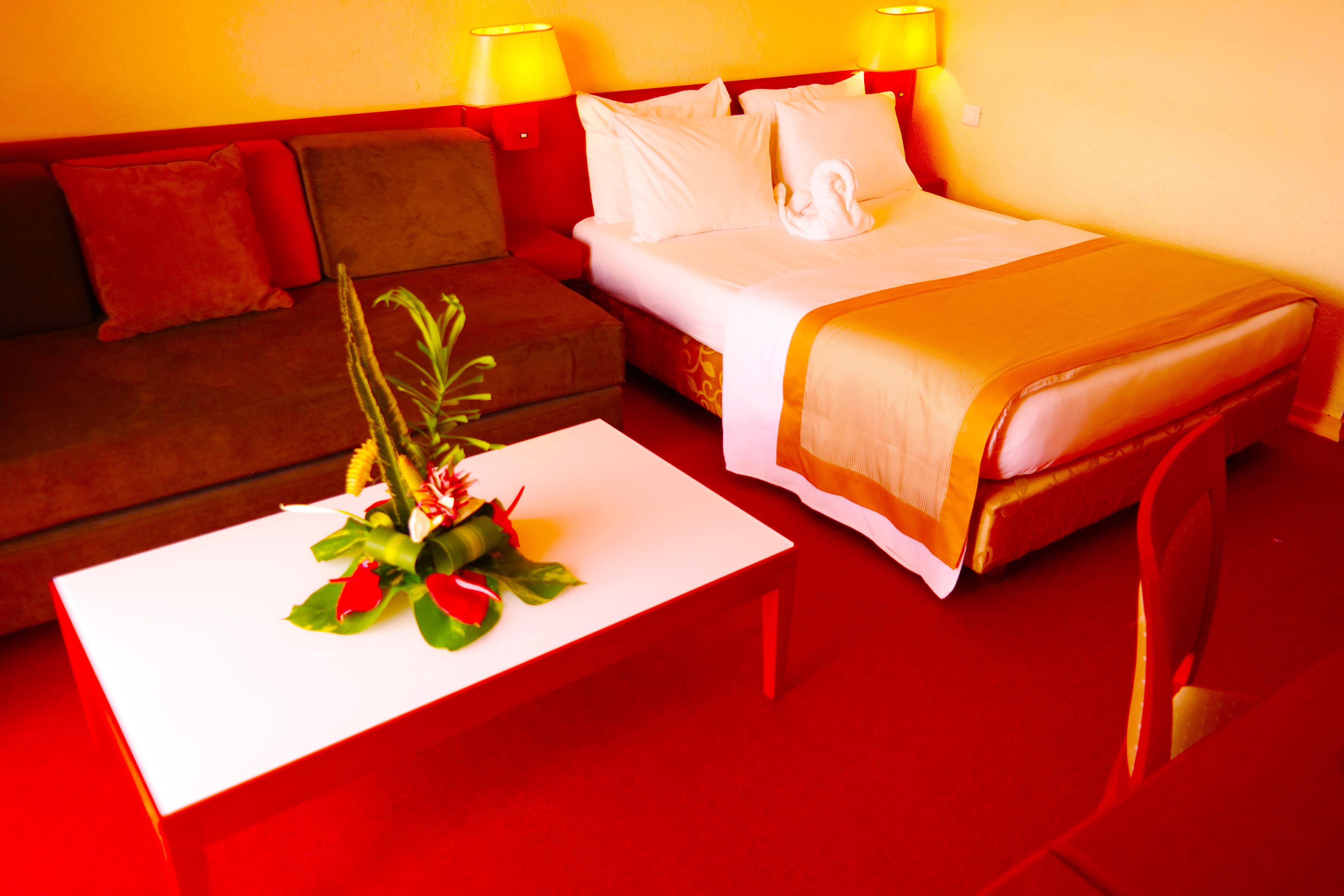 Habitación de hotel con cama, sofá, una mesita con un arreglo floral y dos lámparas de noche.