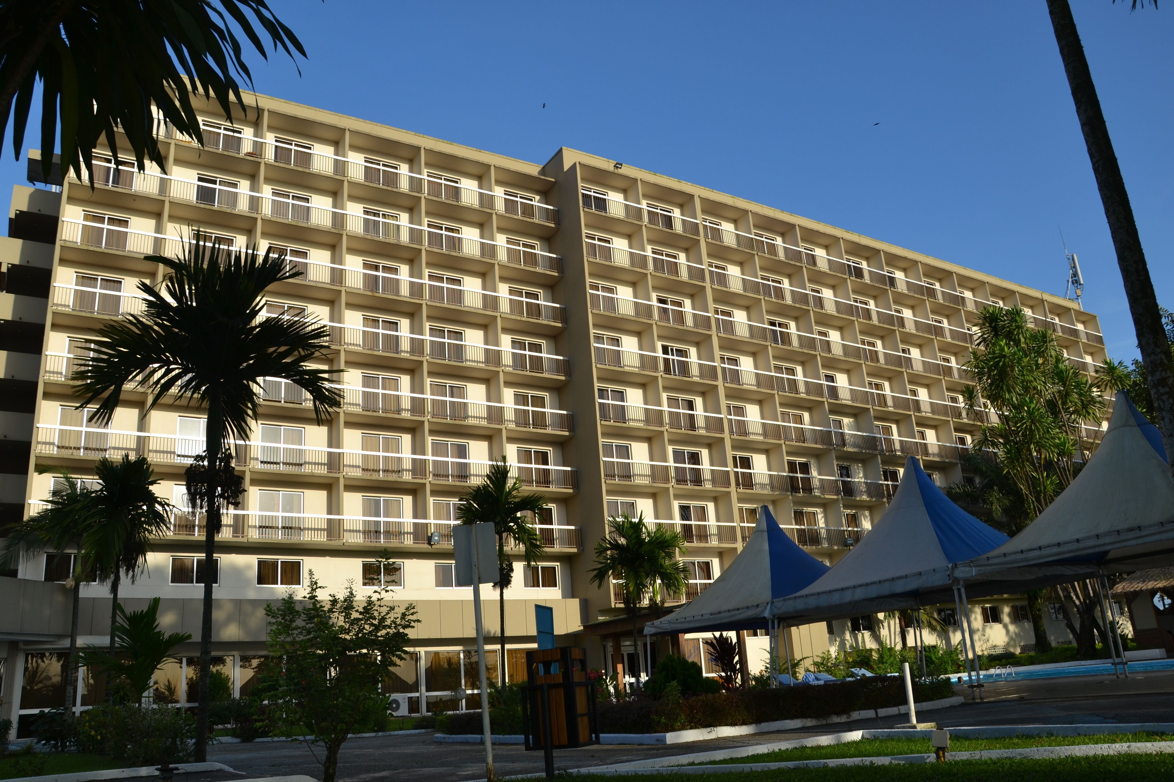Un hotel de varios pisos con balcones, zona de estacionamiento y palmeras.