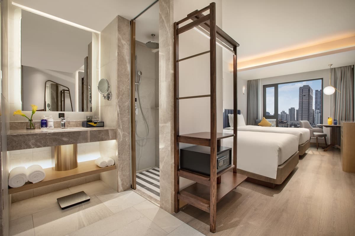 A modern hotel room with a bed, a desk, a shower, and a city view.