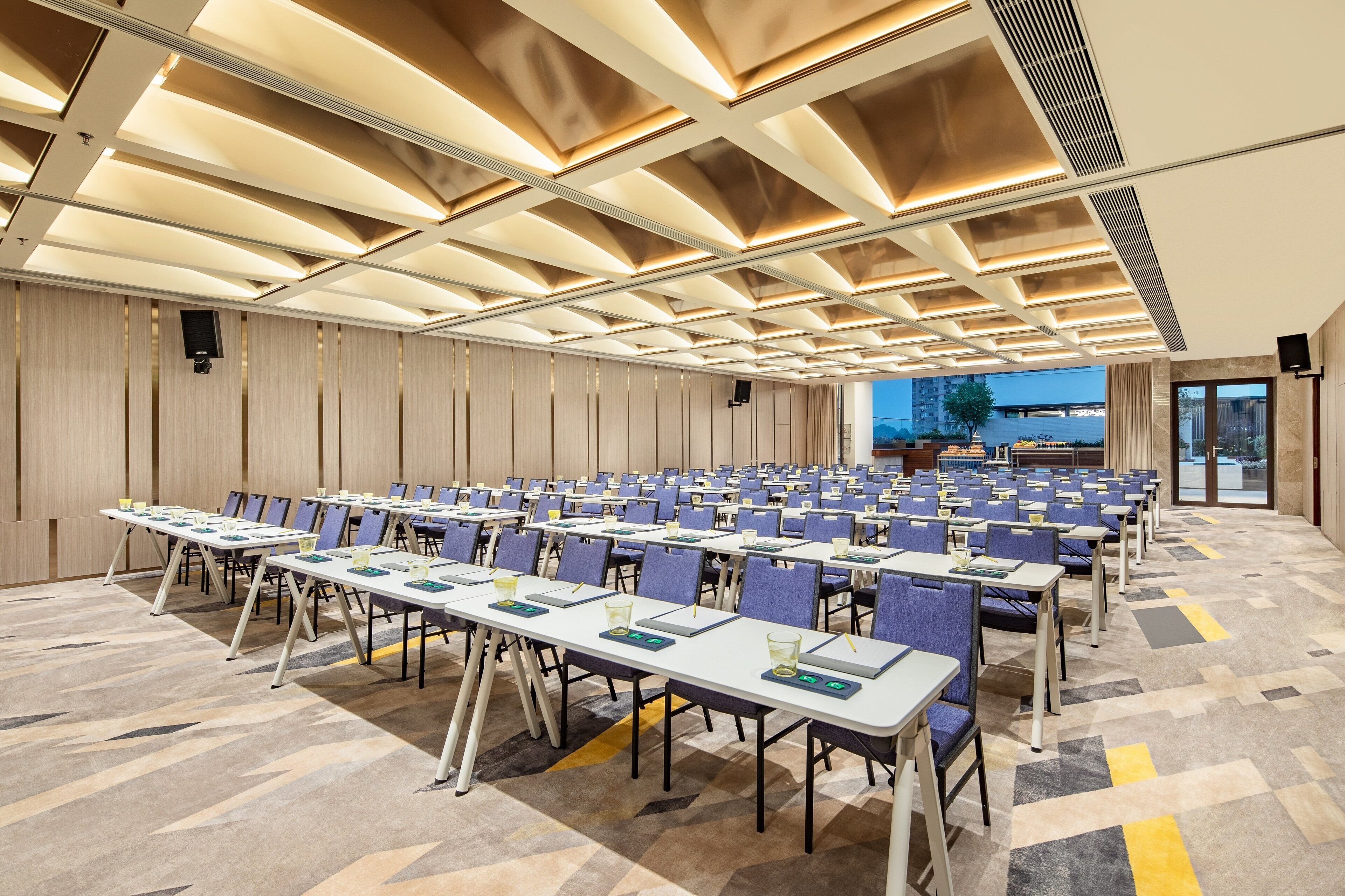 A conference room with rows of tables and chairs, a patterned carpet, and a ceiling with recessed lighting.