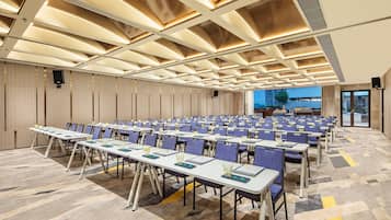 A conference room with rows of tables and chairs, a patterned carpet, and a ceiling with recessed lighting.