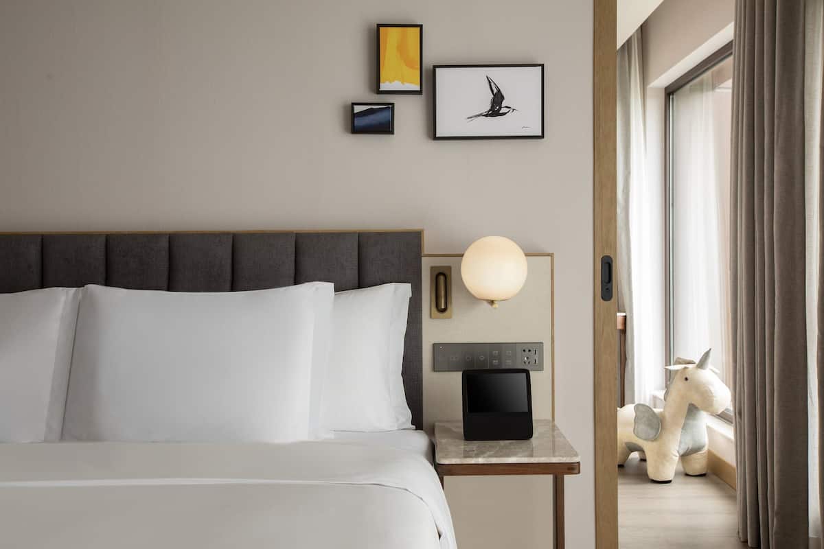 A hotel room with a large bed, a bedside table with a lamp, and artwork on the wall.