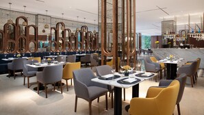 Un restaurante moderno con techos altos, paredes espejadas y diversas opciones de asientos, incluyendo mesas y cabinas.
