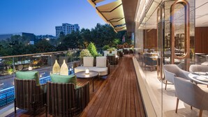Una terraza en la azotea con mobiliario exterior, vistas panorámicas de la ciudad y una barandilla de cristal.