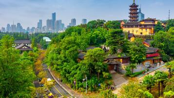 A traditional building with a pagoda-style tower, surrounded by lush greenery and a modern city skyline in the background.