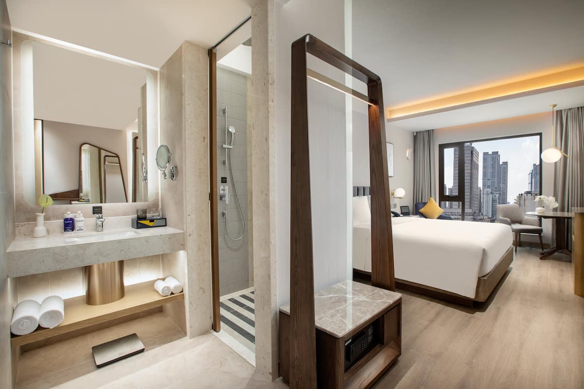 A modern hotel room with a large bed, a bathroom with a shower, and a city view.