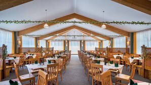 A spacious dining hall with high wooden ceilings, multiple tables and chairs, and large windows allowing natural light. - JUFA Hotel Altaussee (Altaussee)