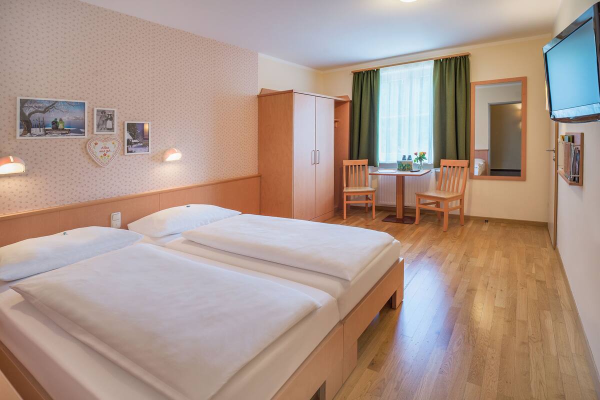 A hotel room with two beds, a desk with chairs, a TV, and a window with curtains.