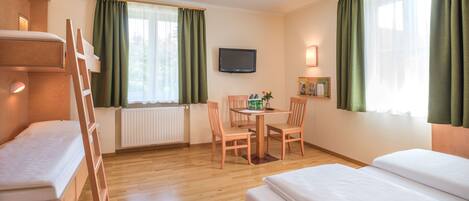 A hotel room with a bunk bed, a desk with chairs, a television, and a window with curtains.
